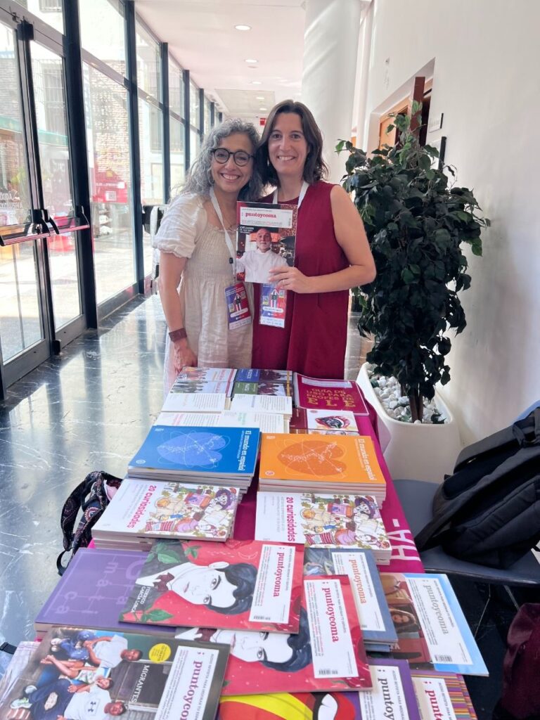 Language educators standing beside a table of story-based reading materials for intermediate level learners. 
